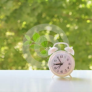 A clock in a white plastic case with a white dial with black hands and numbers stands on a white surface in the garden