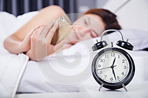 Clock with woman using her smartphone on bed