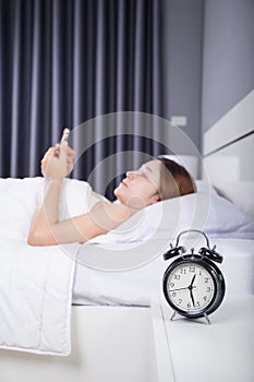 Clock with woman using her smartphone on bed
