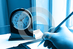 Clock and writing hand on note