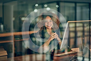 Clocking in some overtime overnight. Portrait of a happy young businesswoman using a computer during a late night at