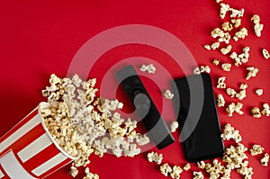 Cloeup of stripped box full of pop corn and black tv remote control on the red background