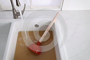 Clogged kitchen sink with plunger and dirty water