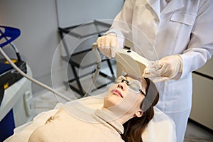 Clos-up woman getting facial laser treatment for hair removal, skin smoothing and age and pigments spots treatment on her face in