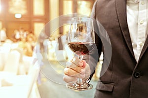 Close of of business man wearing suit holding a glass of wine in the company party with ray yellow light in the background.