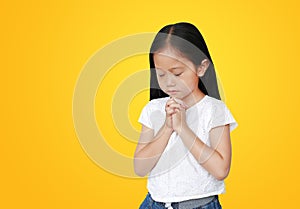 Close eyes beautiful little asian child girl praying isolated on yellow background with copy space. Spirituality and religion