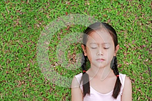 Close eyes little Asian child girl with two ponytail hair lying on green grass in the garden