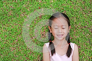 Close eyes little Asian child girl with two ponytail hair lying on green grass in the garden