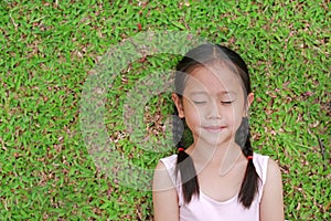 Close eyes little Asian child girl with two ponytail hair lying on green grass in the garden