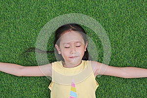 Close eyes little Asian child girl with two ponytail hair lying on green grass in the garden