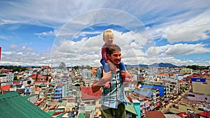 Close Father Holds on Shoulders Little Girl on Roof in City