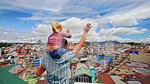 Close Father Holds on Shoulders Little Girl on Roof in City