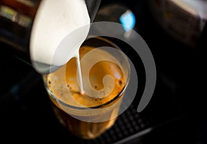 Close focus on pouring steam milk into shot of hot espresso coffee on glass cup