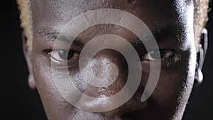 Close footage of dark-skinned blond man`s eyes looking at camera, isolated on black background