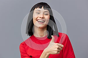 a close horizontal photo of a happy, joyful woman standing on a gray background and showing a big scumbag up in a sign