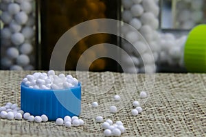 Close image of Homeopathic granules in small bottle cap and some pills scattered on the jute sack surface with blurred white sugar