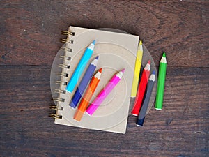 Close note book and color pencil on wooden background