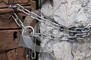 Closed padlock and metal chain at wooden door