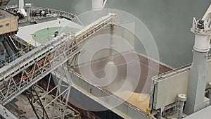 Close panorama of ship loading grain crops on bulk freighter via trunk to open cargo holds at silo terminal in seaport