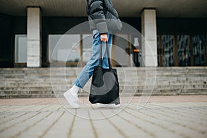 Close photo of female legs in sneakers with a bag in hand on a walk