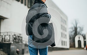 Close photo of a woman in a warm black jacket and with an eco bag in her hands walking down the street on a cloudy autumn day