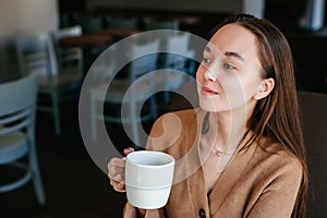 Close portrait of an attractive beautiful girl holding and drinking a cup of coffee in her hand and smiling