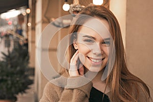 Close portrait of an attractive stylish girl wearing a beige coat, looking into the camera and smiling against the backdrop of the