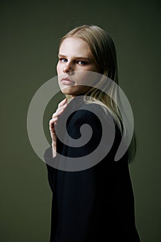 A close portrait of a blonde looking over her shoulder in a black jacket posing in a studio on a green background. The