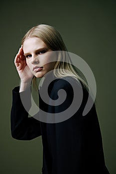 A close portrait of a blonde looking over her shoulder in a black jacket posing in a studio on a green background. The