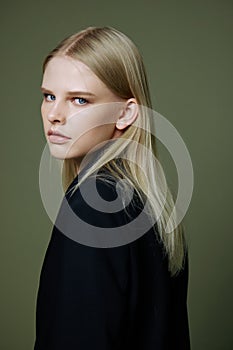 A close portrait of a blonde looking over her shoulder in a black jacket posing in a studio on a green background. The