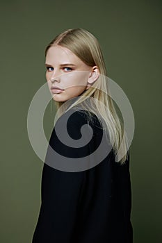 A close portrait of a blonde looking over her shoulder in a black jacket posing in a studio on a green background. The