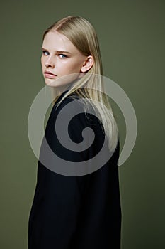 A close portrait of a blonde looking over her shoulder in a black jacket posing in a studio on a green background. The