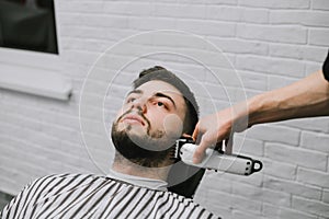 Close portrait of a client lying in a barber shop chair and looking up while cutting his hair. The barber cuts the beard of an