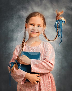 Close portrait of a happy girl kid with two flying braids on a gray background with book