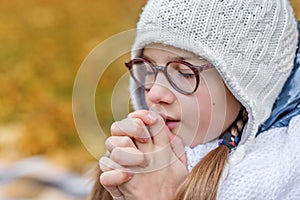 close portrait of little beautiful cute girl teenager with glasses and cozy scarf praying makes a wish