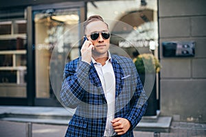 Close portrait a man. stylish young guy talking on the phone wearing a blue jacket white shirt and sunglasses. busy