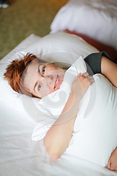 Close portrait of Redhead relaxing sleeping adult woman lies in white bed and smiles at camera