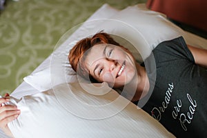 Close portrait of Redhead relaxing sleeping adult woman lies in white bed and smiles at camera