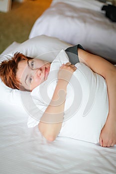 Close portrait of Redhead relaxing sleeping adult woman lies in white bed and smiles at camera
