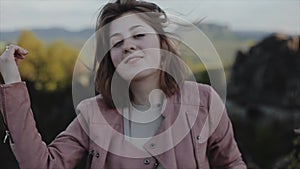 Close portrait view of a beautiful smiling young woman in front of blurred mountainous view. Slow motion