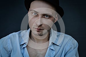 Close portrait of a young bald man with blue eyes and a black hat looking intently at the camera