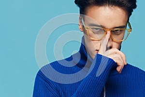 a close portrait of a young man in a blue jacket with yellow eyeglasses, holding them with his index finger, looks at