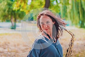 Close portrait of a young red-haired woman in a green park with a saxophone