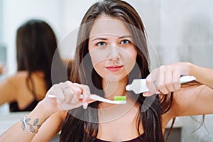 Close is portrait of young woman holding toothpaste and a toothbrush. Feemale look into camera and smile with a snow