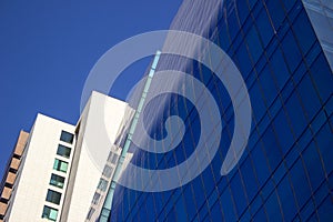 Close shot of a curved blue glass window wall of a modern and elegant corporative building, next to a yellowish classical one.