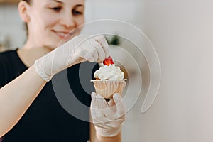 Close shot of many sweet cupcakes on the foreground while a baker decorating the last one.