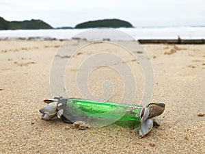 Close shot of old green plastic lighter covered with shells on a beach