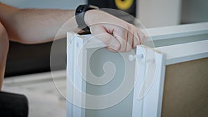 A close shot at the repairman`s hands, the man uses a hammer and plastic nails, in order to collect the shelves from the