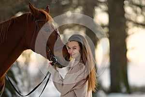 Close side portrait of young smiling woman and brown horse. Woman with long hear hugging horse