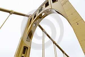 Close structural details of a self anchored suspension bridge painted yellow, overcast sky